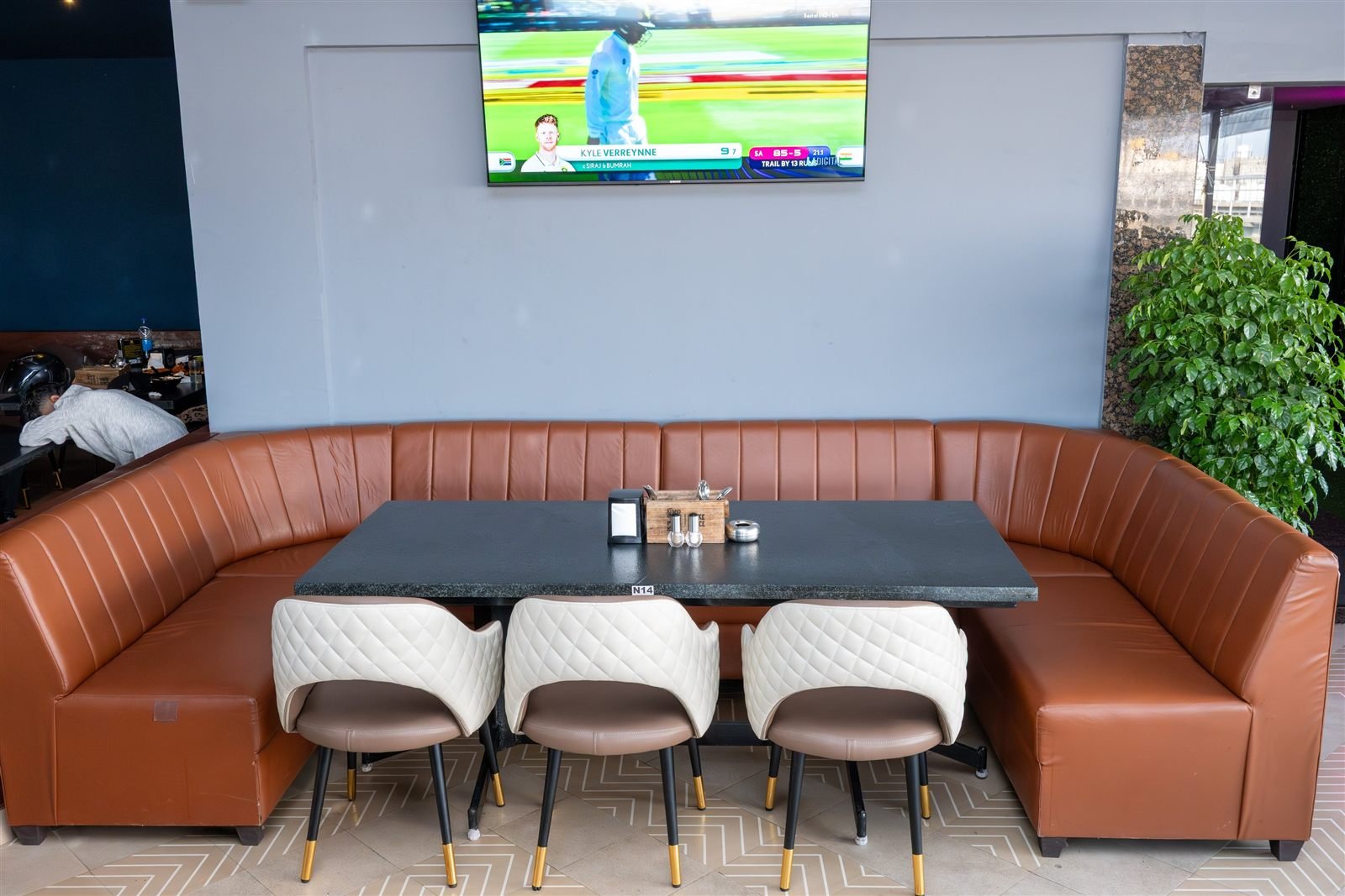 A leather booth beneath a television showing cricket