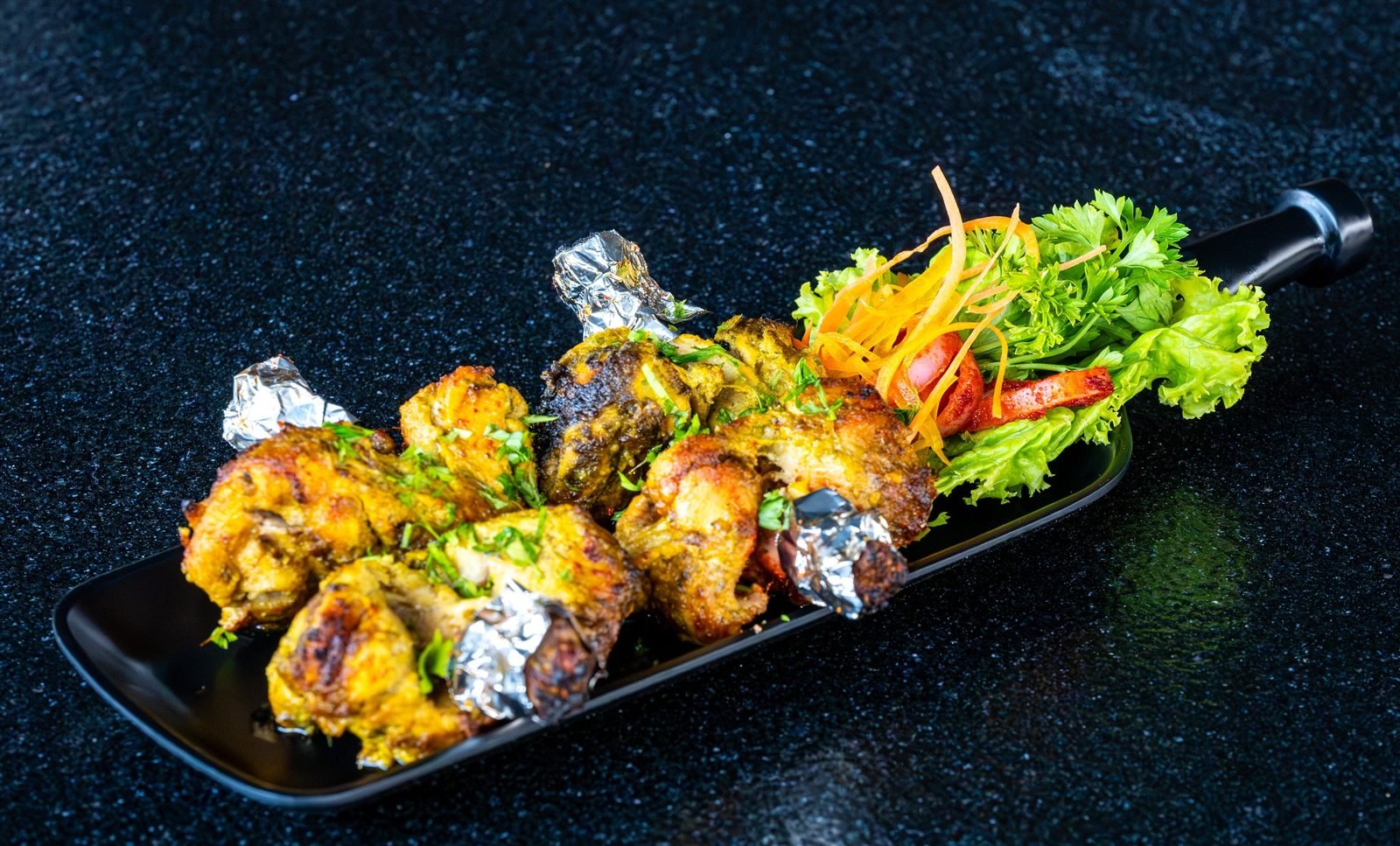 Grilled chicken pieces with foil-wrapped ends on a long platter