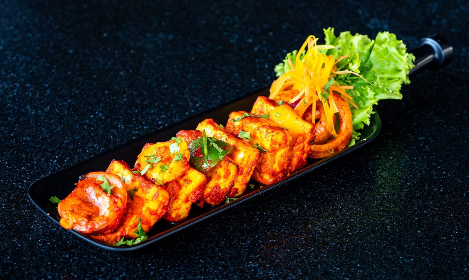Grilled paneer and vegetables served on a long black platter
