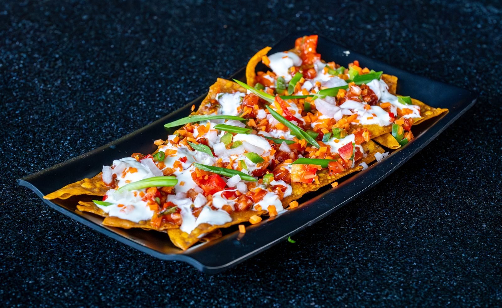 A loaded platter topped with sauce, tomato and spring onion