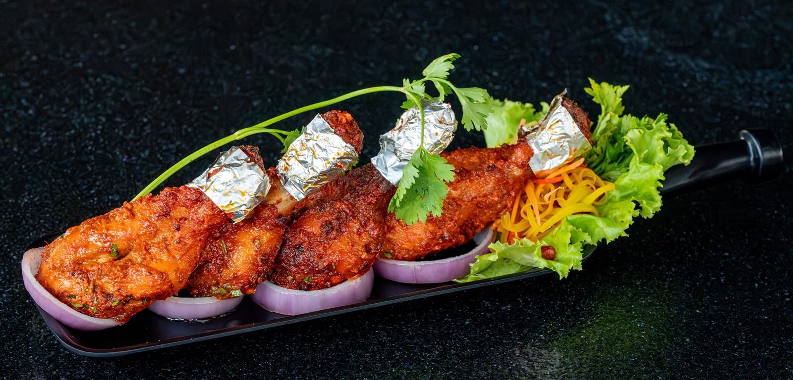 Chicken leg kababs with foil-wrapped ends and salad