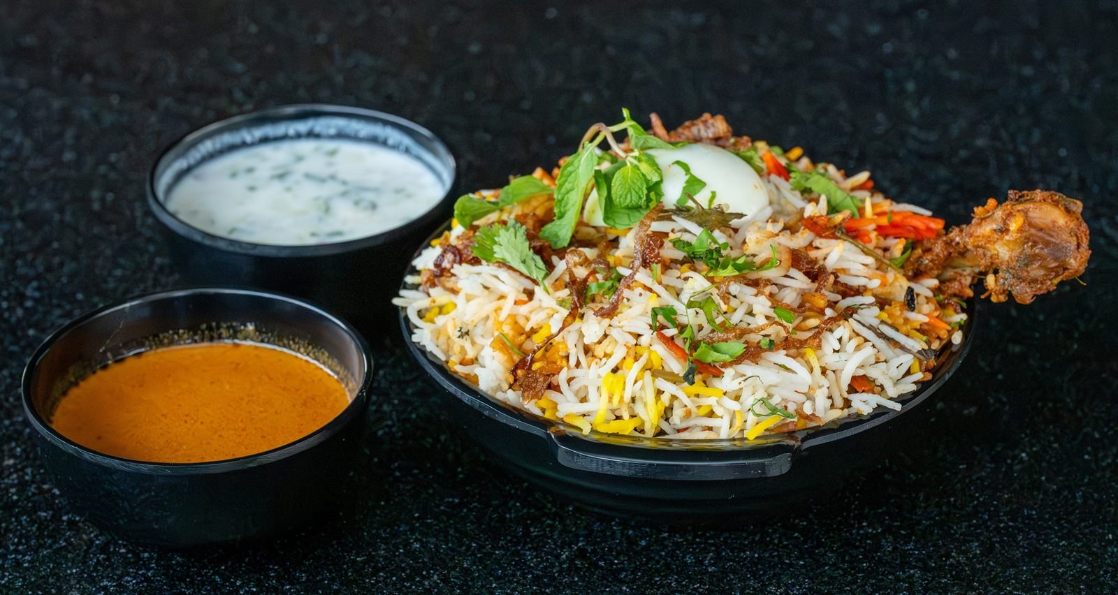 A bowl of biryani served with raita and gravy