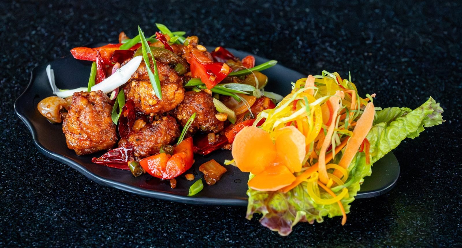 A saucy fried starter with peppers and a salad garnish
