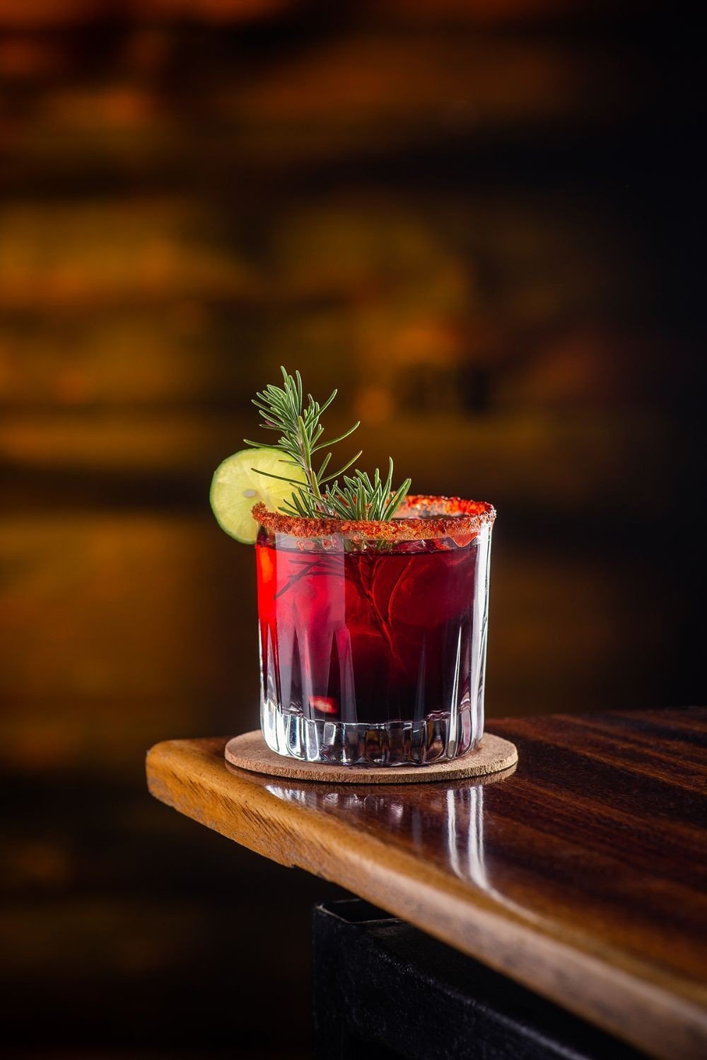 A red cocktail garnished with rosemary and lime on the bar